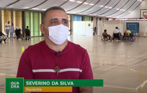 De camisa vermelha, o paciente e jogador de rugy em cadeira de rodas Severino da Silva fala sobre sua reabilitação. Ao fundo, na quadra poliesportiva do Hospital SARAH Lago Norte, outros cadeirantes conversam em grupos.