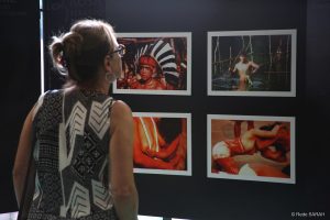 De pé, mulher examina fotografias de indígenas brasileiros, coladas em um mural, como parte de exposição fotográfica no SARAH Brasília.
