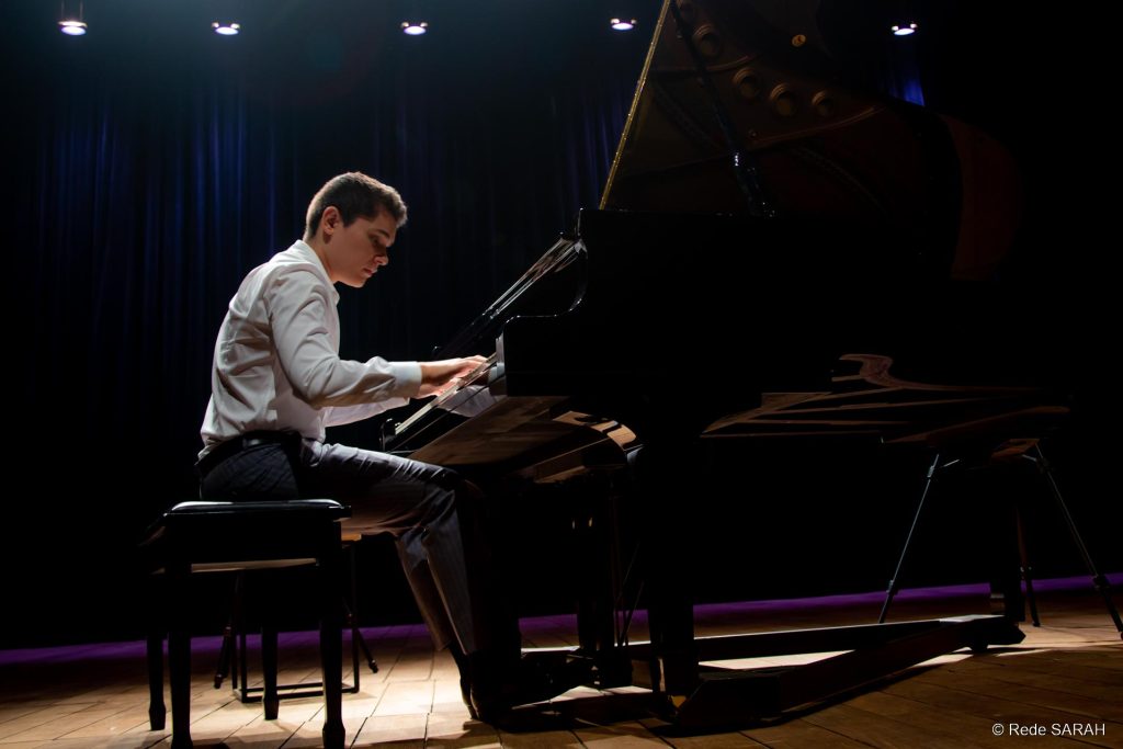 Trajando camisa e calça sociais cinza e sentado ao piano de cauda, o pianista Aleyson Scopel apresenta-se no Teatro SARAH.