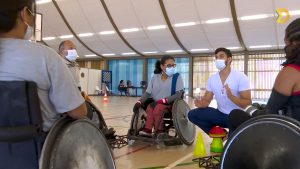 Na quadra poliesportiva do SARAH Lago Norte, professor de educação física, sentado, dá aula de rugby a paratletas, sentados em cadeiras de rodas.