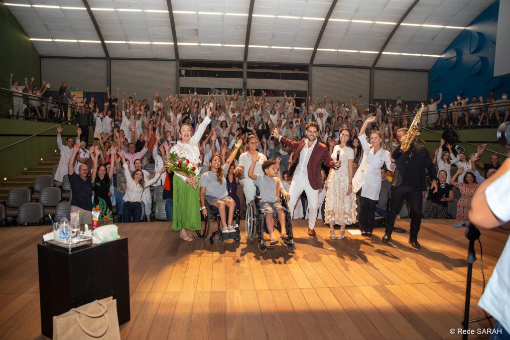 Thiago Arancam e Angélica Cruz posando para foto junto à Dra. Lúcia Willadino Braga e o público do Teatro SARAH